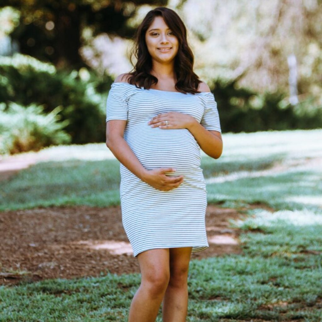 A pregnant woman in a white dress standing on the grass.